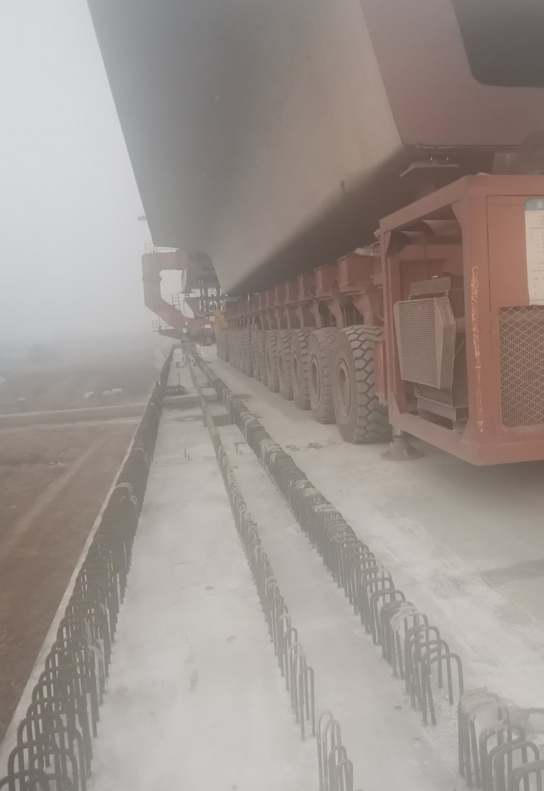 Beam carrier and girder transporter carrying a box girder, axle group visible